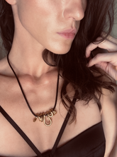 Load image into Gallery viewer, A close-up image of a woman wearing a black leather necklace with a gold-colored snake pendant.