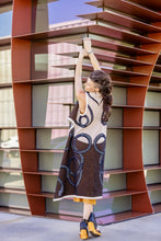 Load image into Gallery viewer, Woman in a stylish dress standing next to a modern architectural structure
