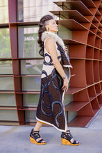 Load image into Gallery viewer, Woman wearing a patterned dress standing in front of a modern architectural structure.