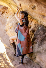 Load image into Gallery viewer, Woman in a patterned dress standing against a rock wall