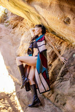 Load image into Gallery viewer, Woman in a colorful dress sitting against a rock wall