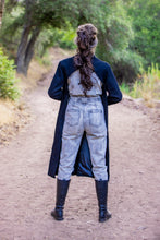 Load image into Gallery viewer, Person wearing a long coat, light-colored pants, and dark boots standing on a dirt path with trees in the background.