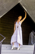 Load image into Gallery viewer, Woman in a light purple dress standing on steps with a modern architectural background