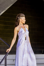 Load image into Gallery viewer, Woman in a light purple dress standing against a dark brick wall.