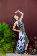 Load image into Gallery viewer, Woman in a patterned dress standing outdoors with plants in the background