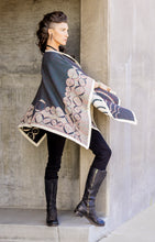 Load image into Gallery viewer, Woman wearing a patterned cape over a dark outfit against a concrete wall.