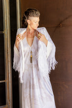 Load image into Gallery viewer, Woman wearing a white dress with fringe and a necklace, standing against a brown wall.
