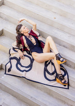 Load image into Gallery viewer, Woman lounging on a large scarf with a pattern, wearing a dress and sandals, on stone steps.
