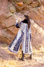 Load image into Gallery viewer, Person wearing a long, patterned coat climbing a rocky wall.
