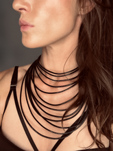 Load image into Gallery viewer, A close-up image of a woman wearing a black leather layered collar necklace with a luminous brass clasp.
