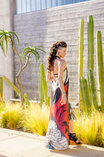 Load image into Gallery viewer, Woman in a colorful dress standing among cacti and plants.
