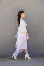 Load image into Gallery viewer, Woman in a white dress with fringe walking against a gray wall
